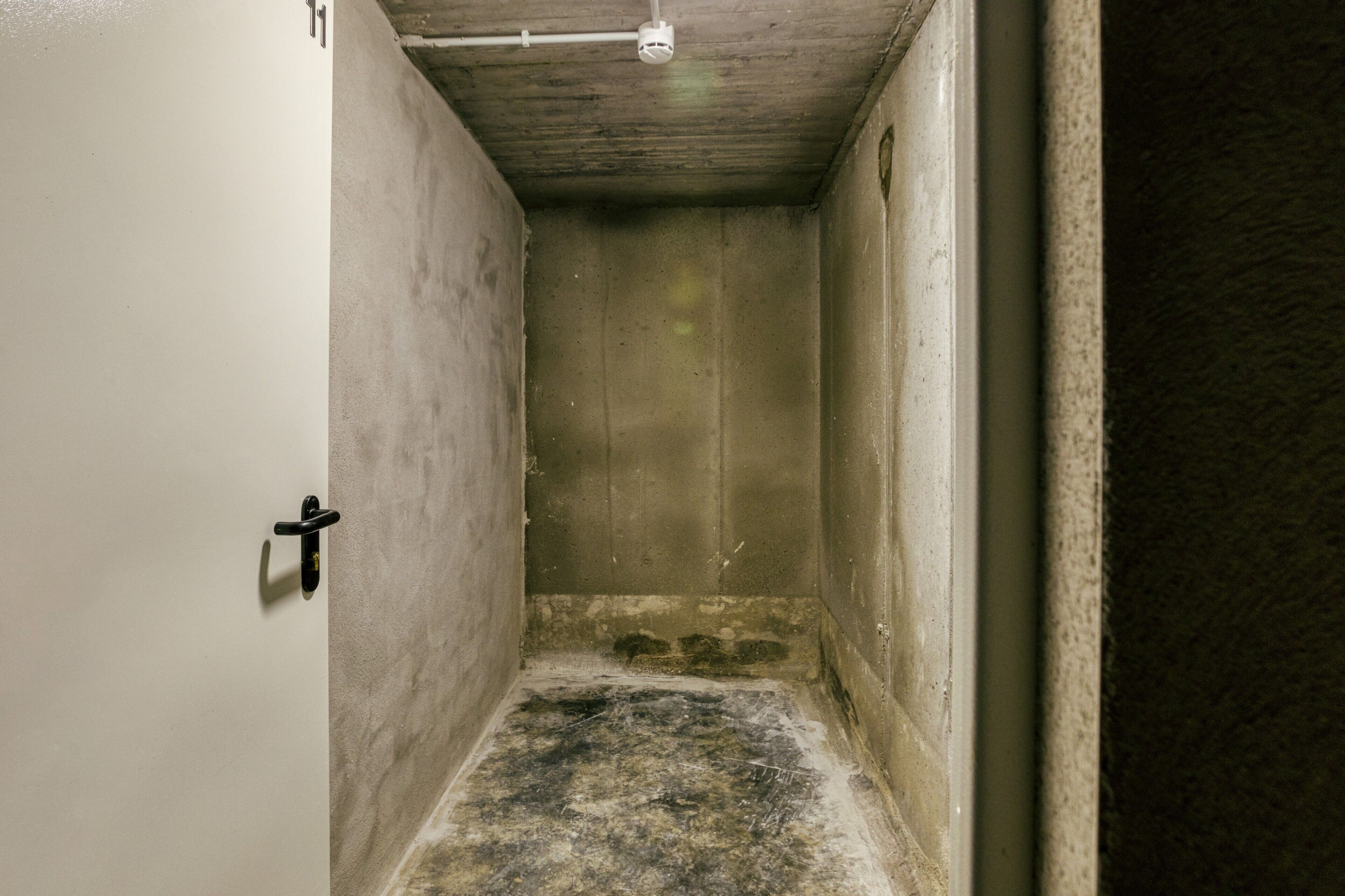 A narrow, dimly lit hallway with a rough, unfinished floor and a door on the left.