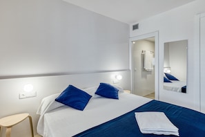 A hotel room with a bed, bedside lamps, a mirror, and a door leading to a bathroom.