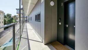 Un pasillo con barandilla de metal, una puerta con el número 2 y una rejilla de ventilación.