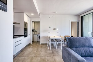 A modern kitchen with white cabinets, a built-in oven, and a dining area with a table and chairs.