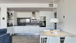 Una cocina moderna con armarios blancos, una mesa de comedor con sillas e iluminación colgante.