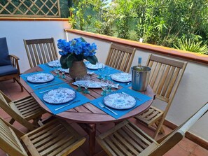 A round wooden table set for six with blue placemats, white patterned plates, and green glassware.