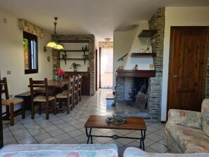 A dining area with a wooden table and chairs, a kitchen with stone walls, a fireplace, and a sofa.