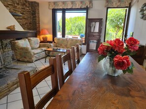 A dining area with a wooden table, chairs, a vase of flowers, a sofa, and a fireplace.