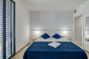A hotel room with a bed, bedside tables, a nightstand, a window with blinds, and a door.
