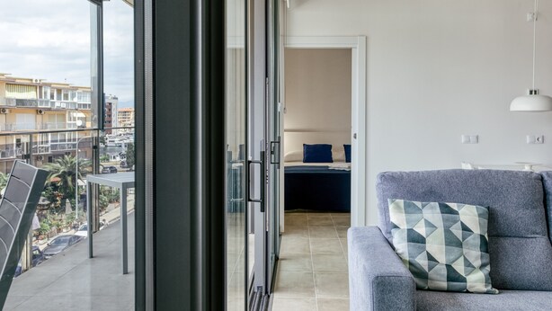 En balkon med udsigt til bygninger, en sofa med et mønstret pudebetræk og en dør til et soveværelse.