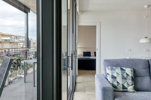 A balcony with a view of buildings, a sofa with a patterned cushion, and a door leading to a bedroom.