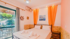 A bedroom with a bed, a window with curtains, a painting, and a small table with a chair. - Family Apartment with Sea View and Shared Pool (Corfu)