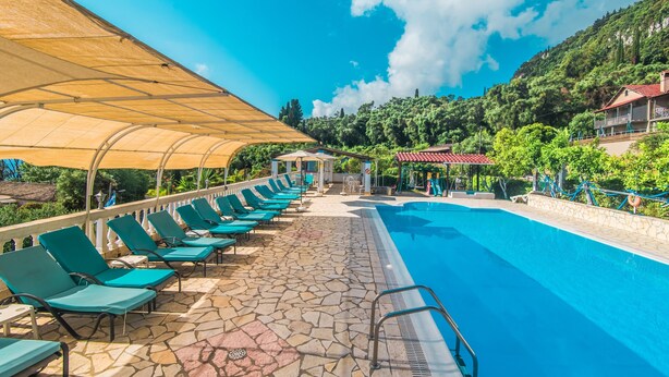 A swimming pool with lounge chairs and a covered area, surrounded by greenery and buildings. - Family Apartment with Sea View and Shared Pool (Corfu)