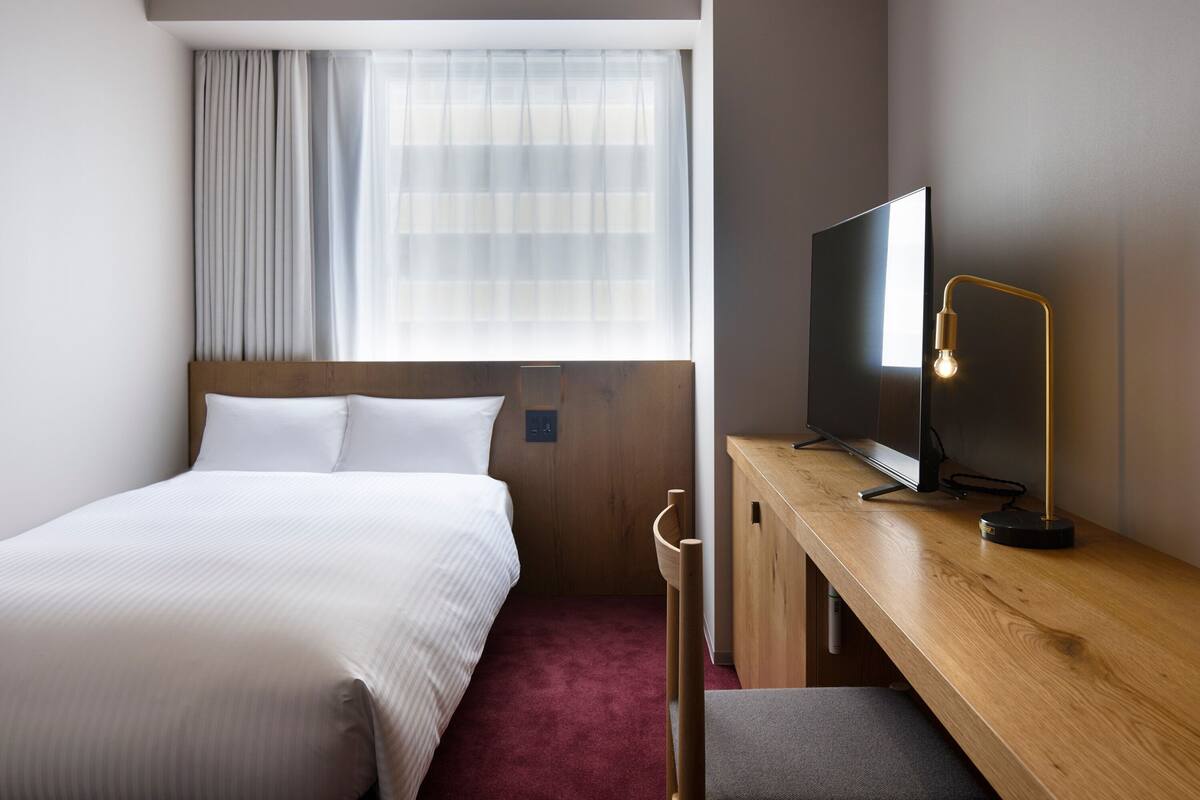 A hotel room with a bed, a desk, a television, and a window with curtains.