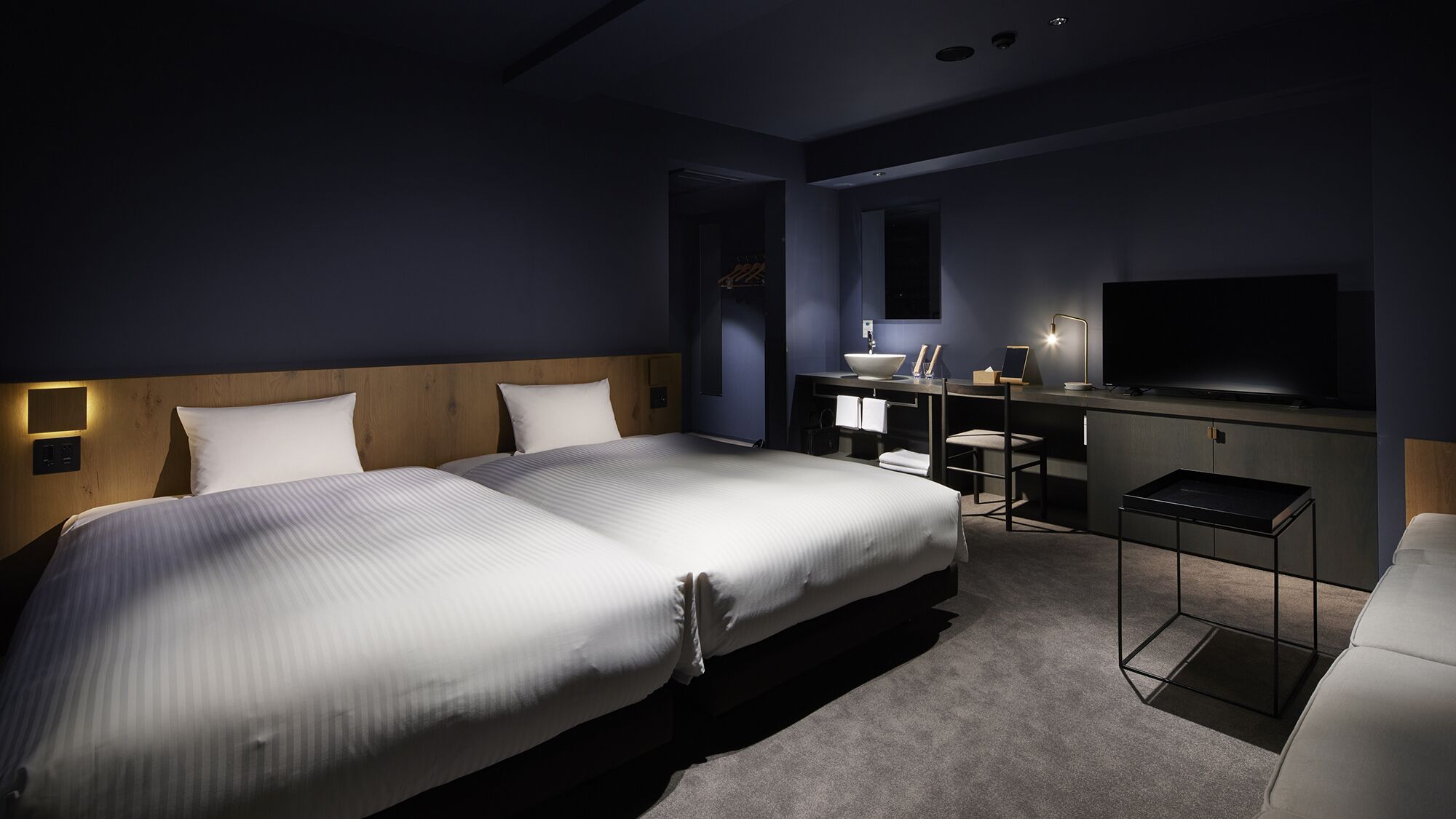 Ein Hotelzimmer mit zwei Betten, einem Schreibtisch, einem Fernseher und einer kleinen Sitzecke.
