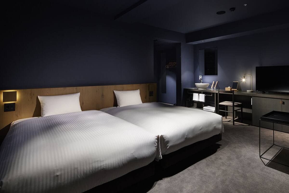 A hotel room with two beds, a desk, a TV, and a small seating area.