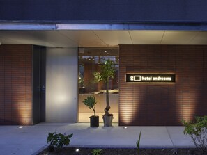 Hotel androoms entrance features a modern design with a clear glass door and potted plants.