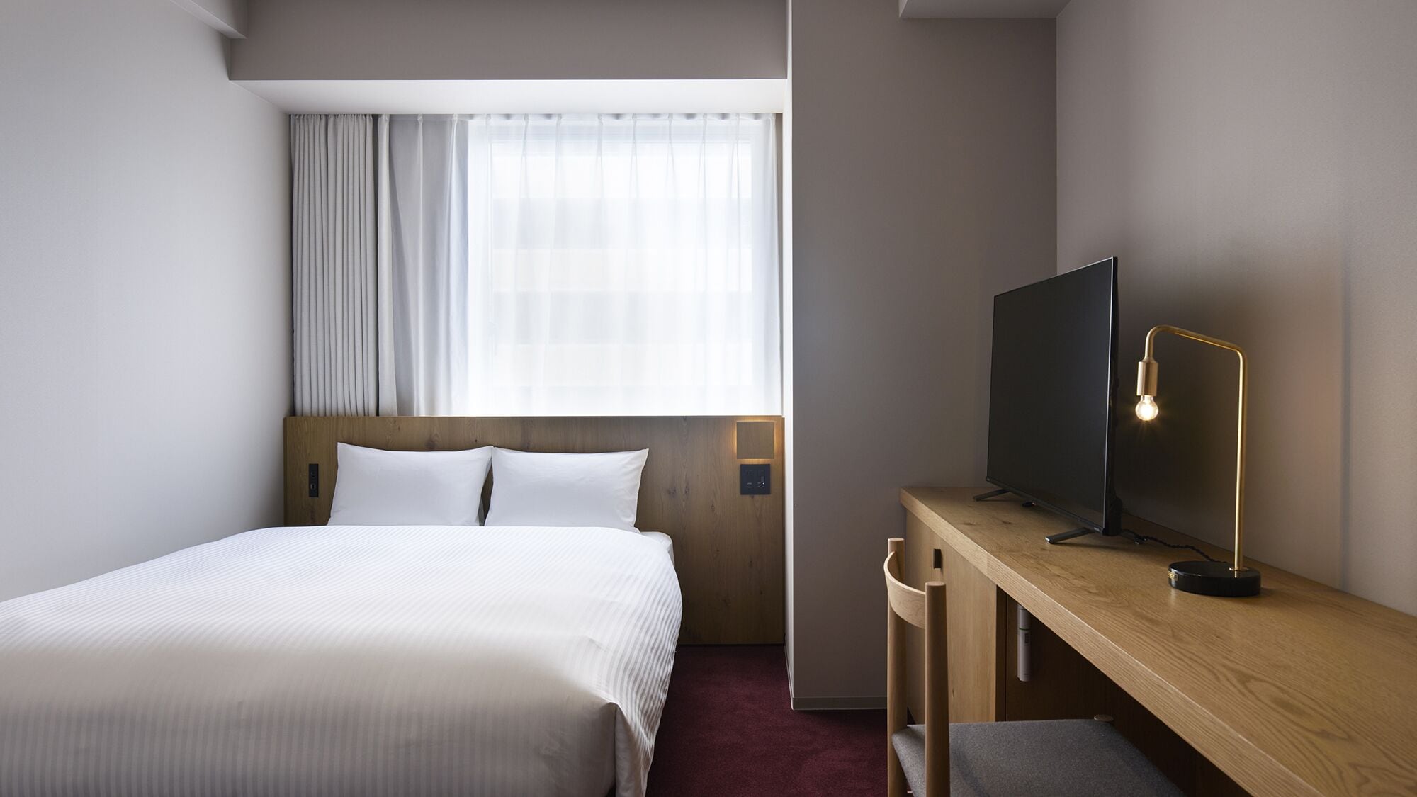 Ein Hotelzimmer mit Bett, Schreibtisch mit Fernseher und Fenster mit Vorhängen.