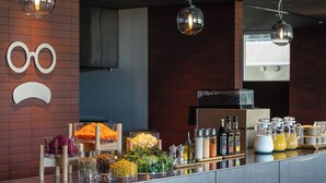 A breakfast buffet with various food items and beverages, a wall with a sad face decoration, and hanging pendant lights. - hotel androoms Sapporo Susukino (Sapporo)