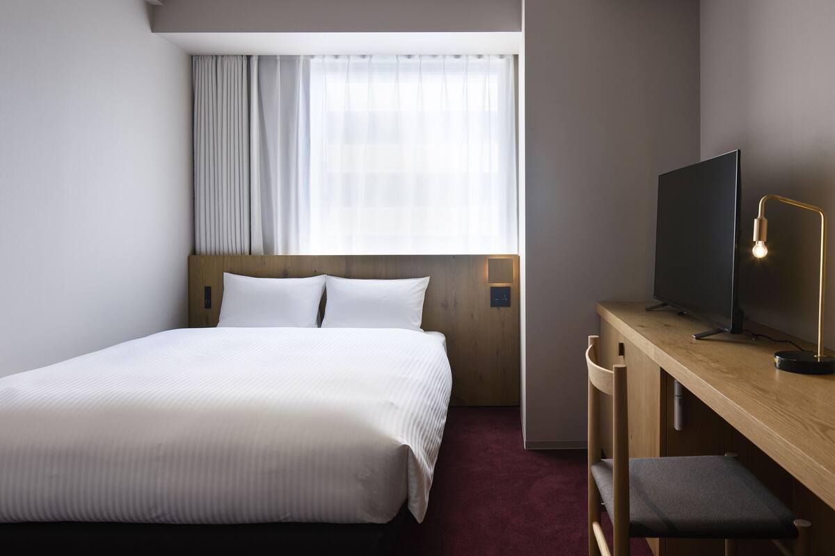 A hotel room with a bed, a desk, a television, and a window with curtains.