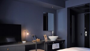 Une chambre d’hôtel moderne dotée d’un grand lit, d’une table de chevet avec une lampe, d’un miroir et d’une salle de bain comprenant un lavabo et un porte-serviettes.