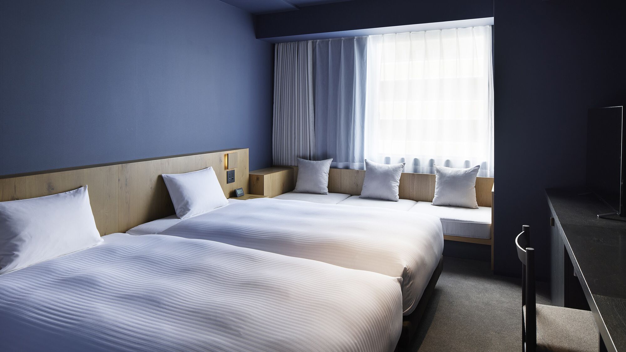 Ein Hotelzimmer mit zwei Betten, einem großen Fenster mit Vorhängen, einem Nachttisch und einem Beistelltisch.
