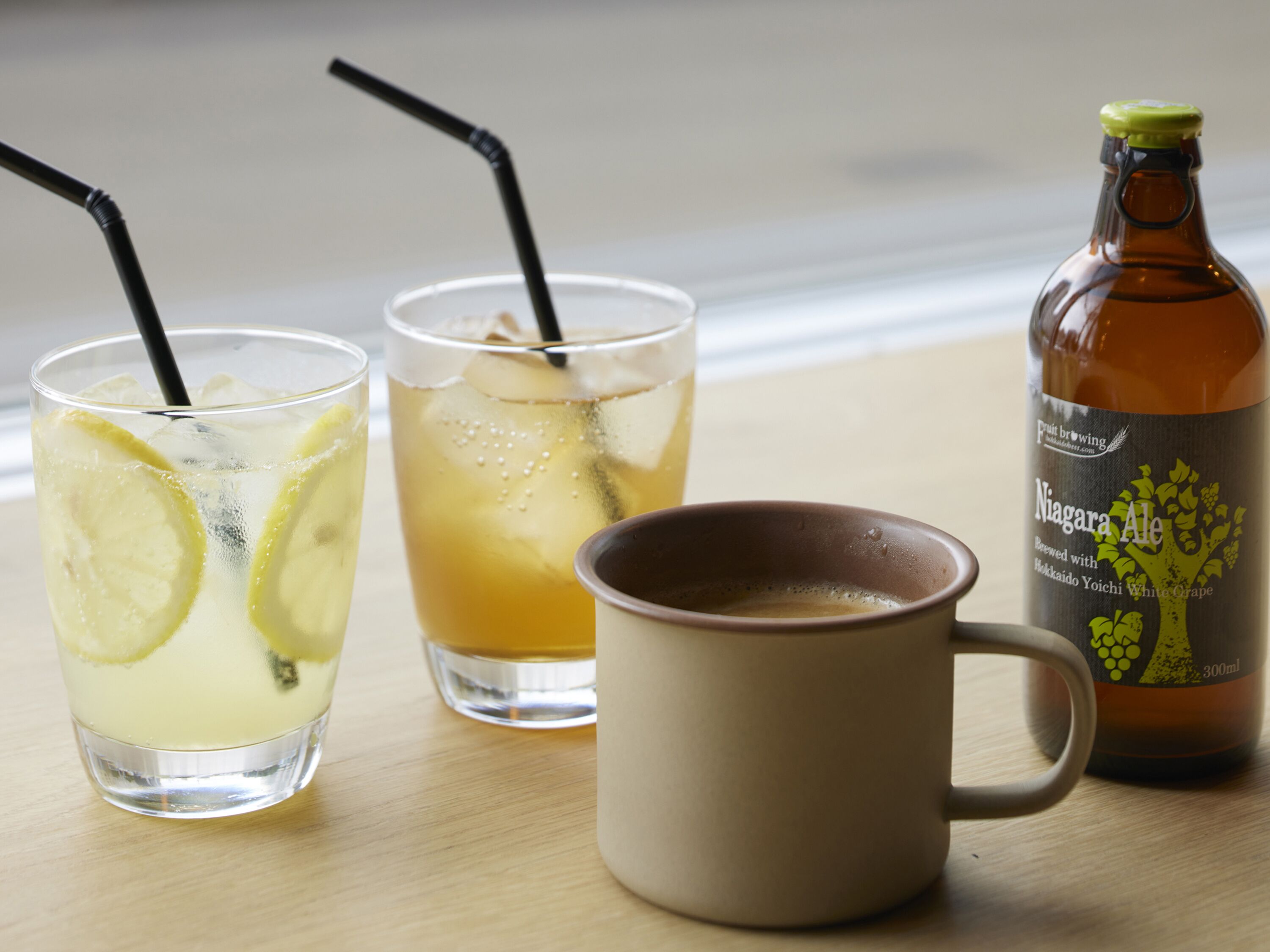Two glasses of beverages with straws and a bottle of beer on a table.