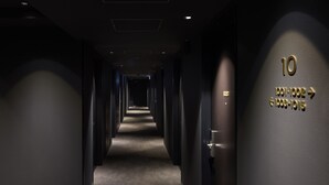 A hotel corridor with a carpeted floor, dark walls, and a sign indicating room numbers 10, 1001-1002, and 1003-1015. - hotel androoms Sapporo Susukino (Sapporo)