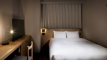 A hotel room with a bed, a desk with a chair, a television, and a nightstand with a lamp.