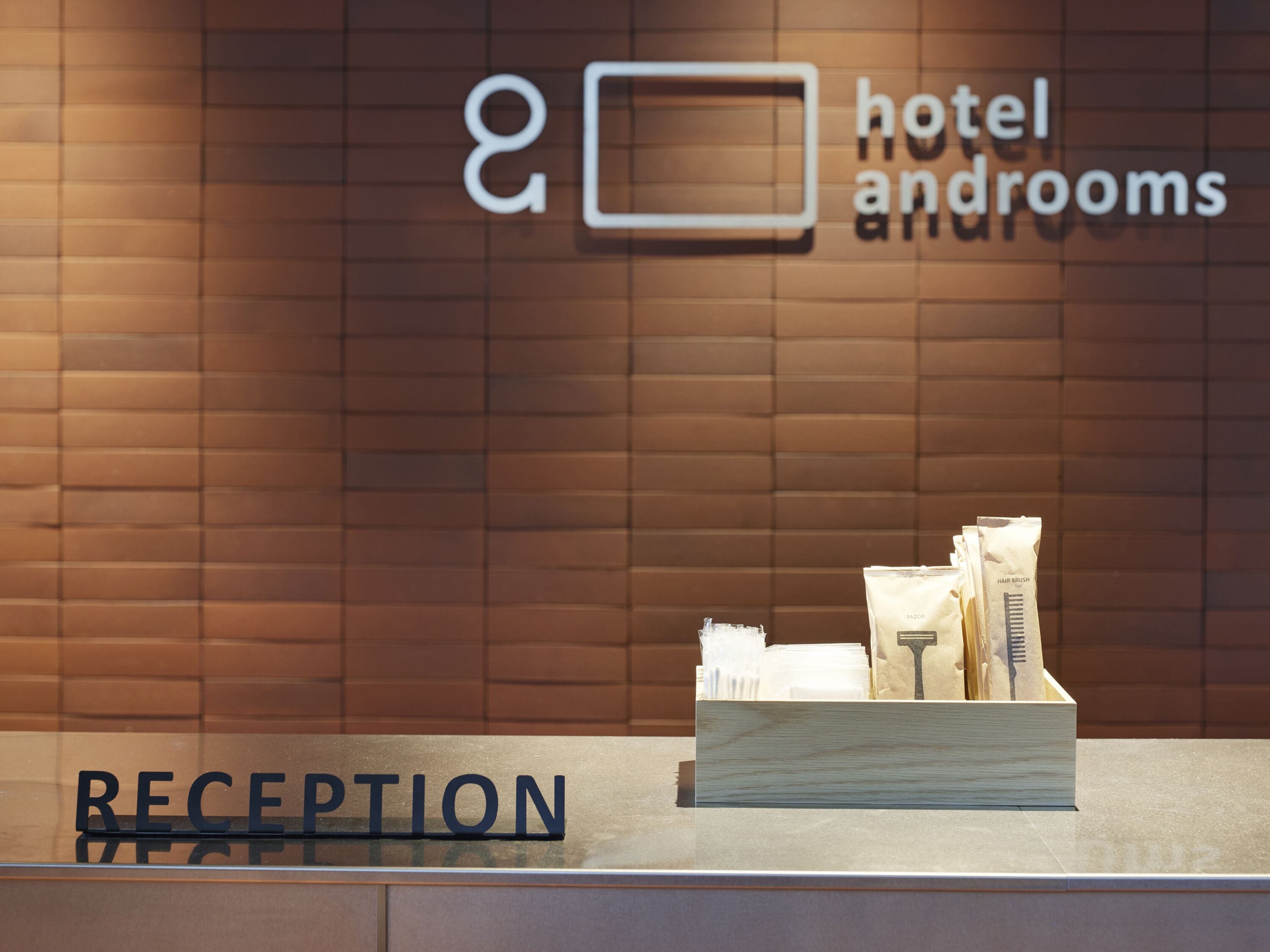 A reception desk with a wooden counter and a sign that reads "RECEPTION". Behind the desk, there is a wall with a sign that says "hotel androoms".