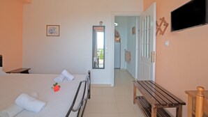A bedroom with a bed, a bedside table, a wooden bench, a TV, and a door leading to another room. - Apartment 'Andromaches Large' with Sea View & Shared Pool (Corfu)
