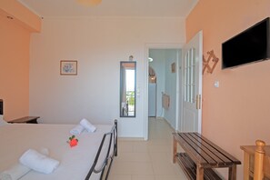 A bedroom with a bed, a bedside table, a wooden bench, a TV, and a door leading to another room.