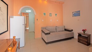 A living room with a sofa, a wooden table, a refrigerator, and a small cabinet. - Apartment 'Andromaches Large' with Sea View & Shared Pool (Corfu)