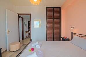 A bedroom with a bed, a bedside table with a flower, a mirror, and a wooden wardrobe.