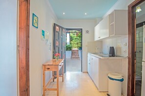 A narrow kitchen with a wooden table, a trash bin, and a view into a garden.