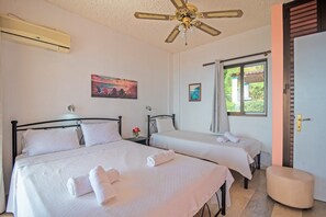 Quarto de hotel com duas camas, um ventilador de teto, ar condicionado, janela com vista e uma porta.