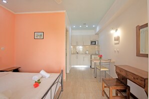 Quarto com cama, escrivaninha e cadeira. Cozinha compacta ao fundo.