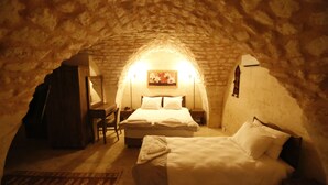 A cozy attic bedroom with a stone ceiling, two beds, a wooden desk, and a framed picture on the wall. - Kaliruha Butik Otel (Sanliurfa)