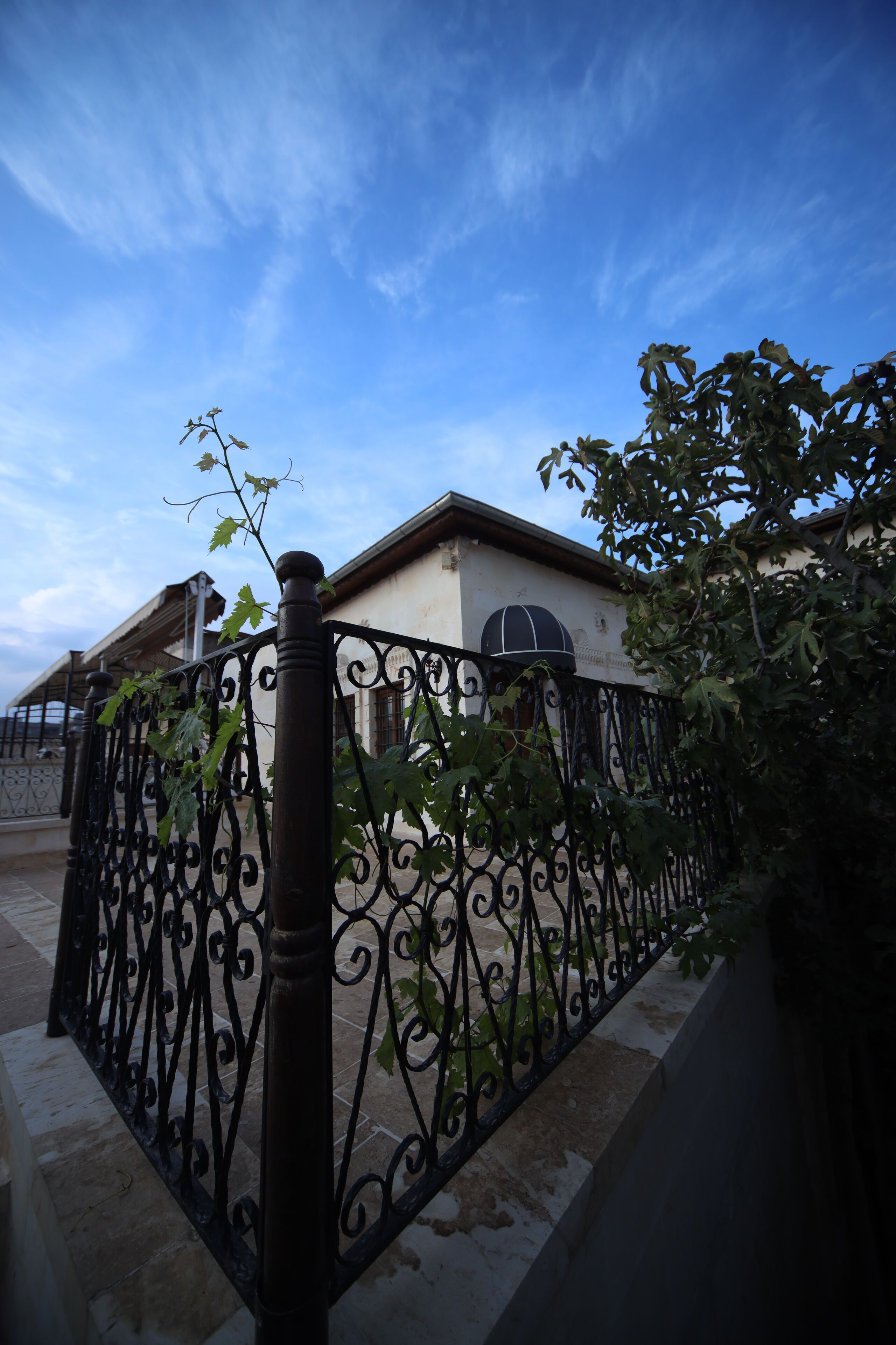A house with a wrought iron fence, a tiled patio, and a clear blue sky.