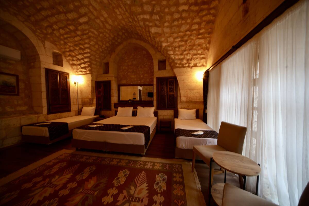 A hotel room with two beds, a chair, a small table, and a large window with curtains.