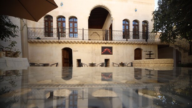 A courtyard with a fountain, seating area, and a building with arched windows and balconies. - Kaliruha Butik Otel (Sanliurfa)