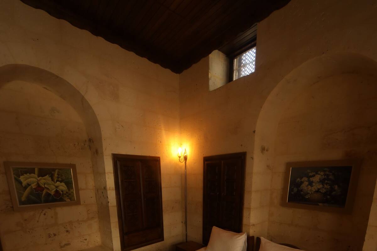 A dimly lit room with a large bed, two wall-mounted lamps, and a small window.