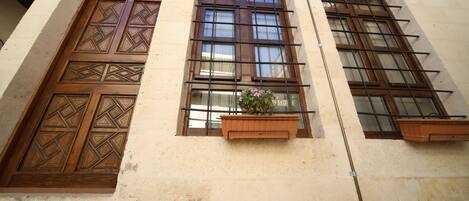 Fachada de edificio con grandes puertas y ventanas de madera, una maceta pequeña con flores y un cartel que dice 'Selamlik'.