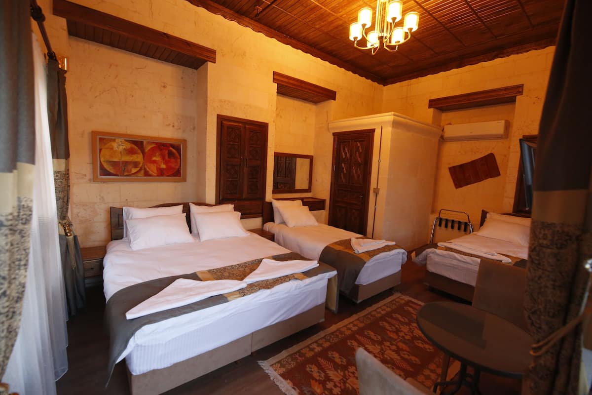 A hotel room with two beds, a desk, and a chair. There is a chandelier, a painting on the wall, and a window with curtains.