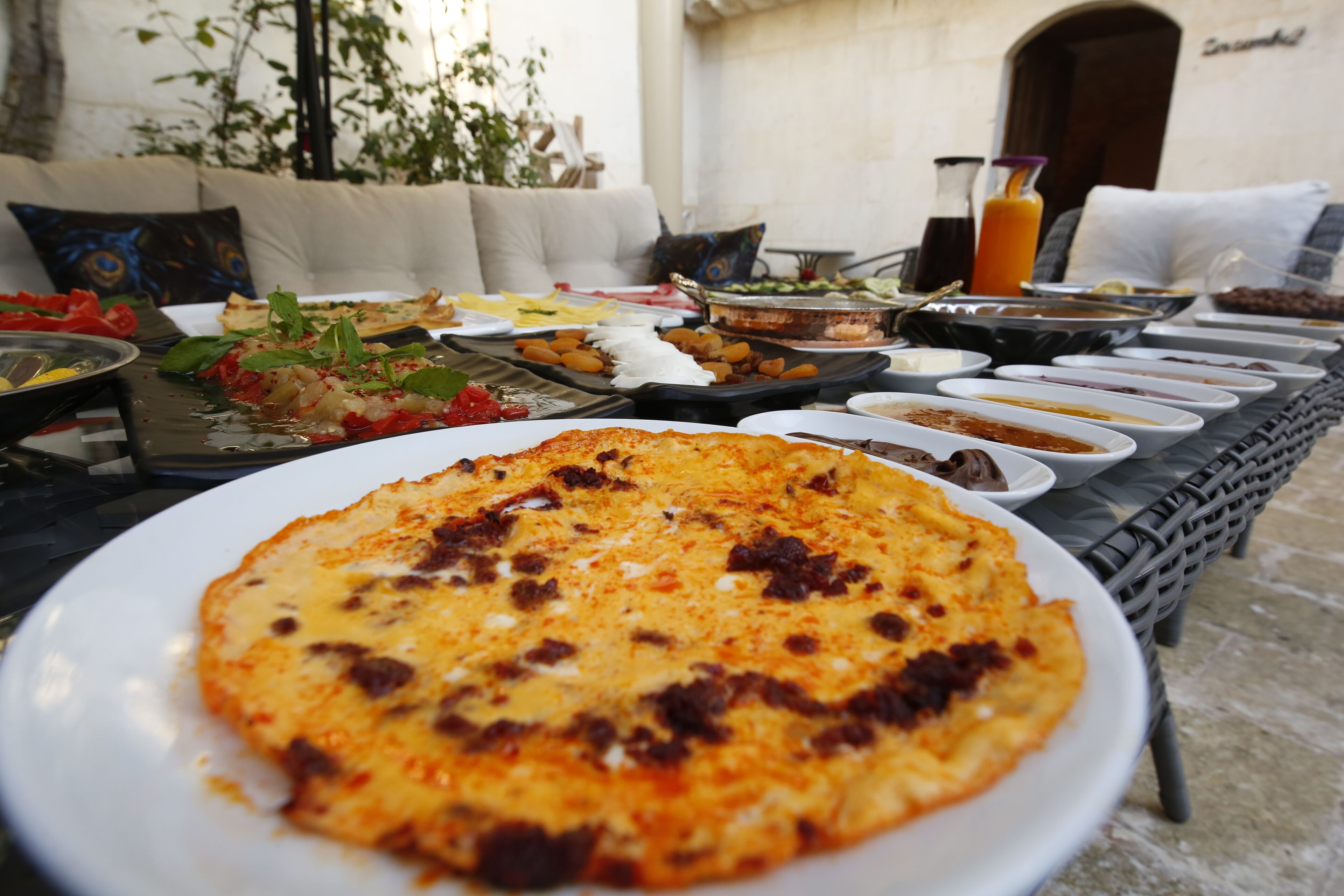A breakfast buffet with various dishes, including a pizza, on a table set outdoors.