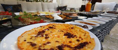 Un bufé de desayuno con diversos platos, incluyendo una pizza, sobre una mesa al aire libre.