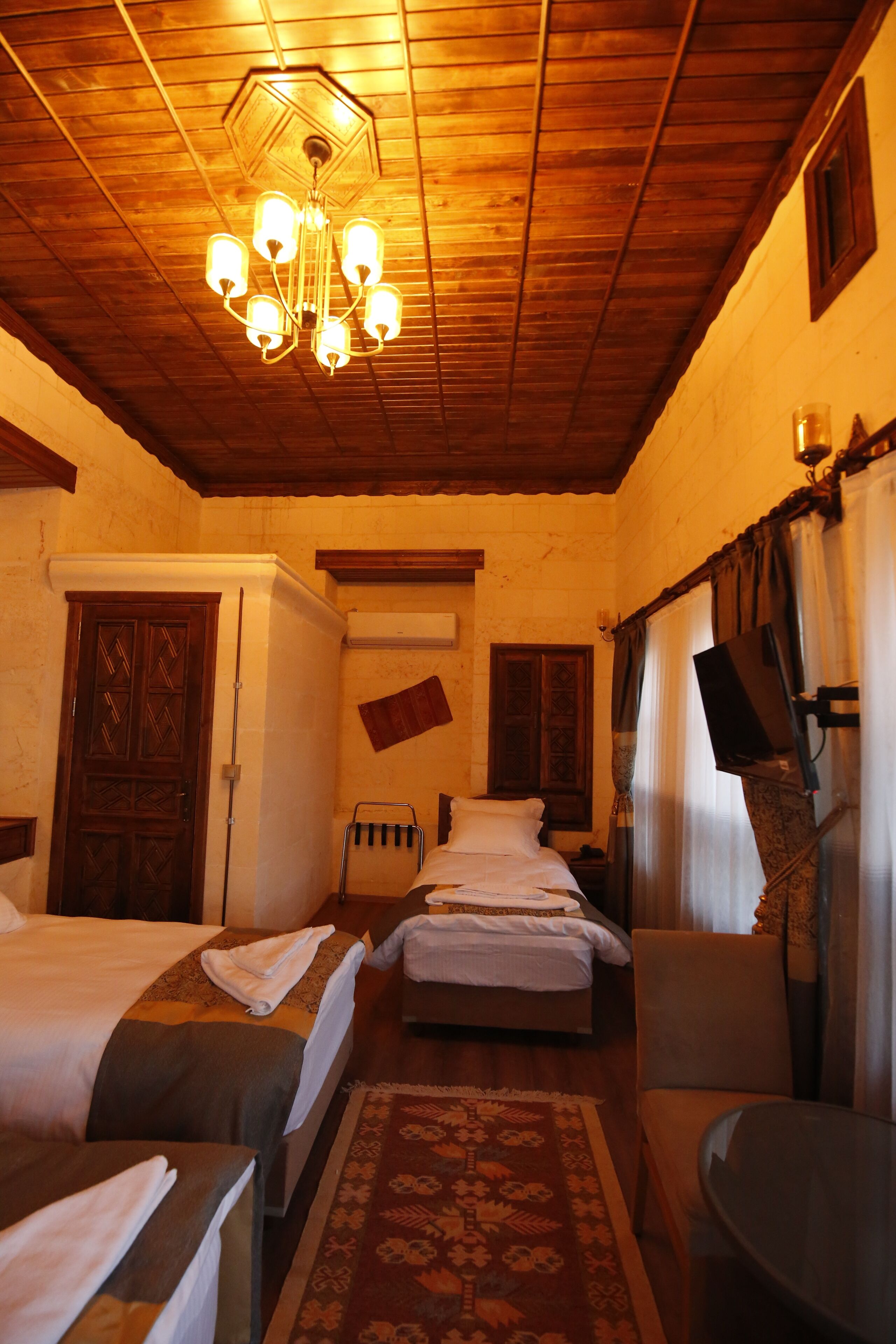 Habitación de hotel con techos de madera, un candelabro, dos camas, una mesita y un televisor.