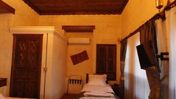 Habitación de hotel con techos de madera, un candelabro, dos camas, una mesita y un televisor.