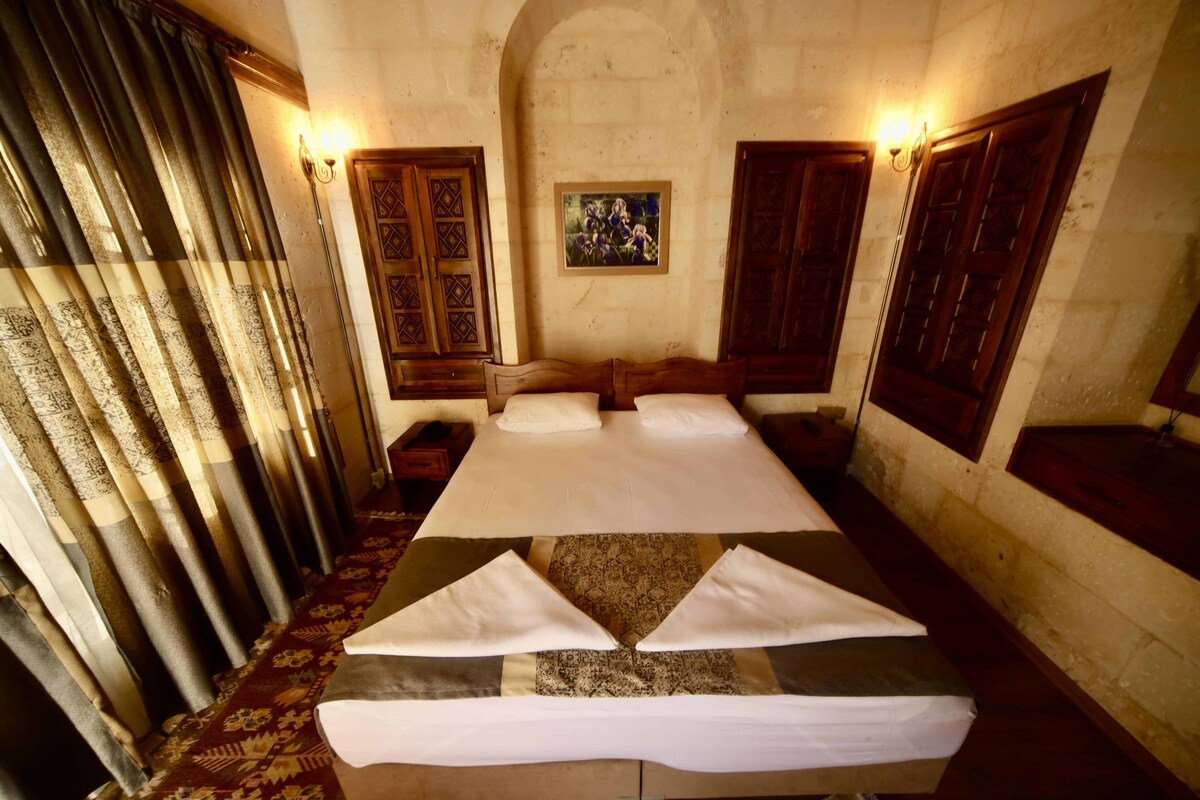 Une chambre avec un grand lit, deux tables de chevet, un tableau au mur et des portes en bois.