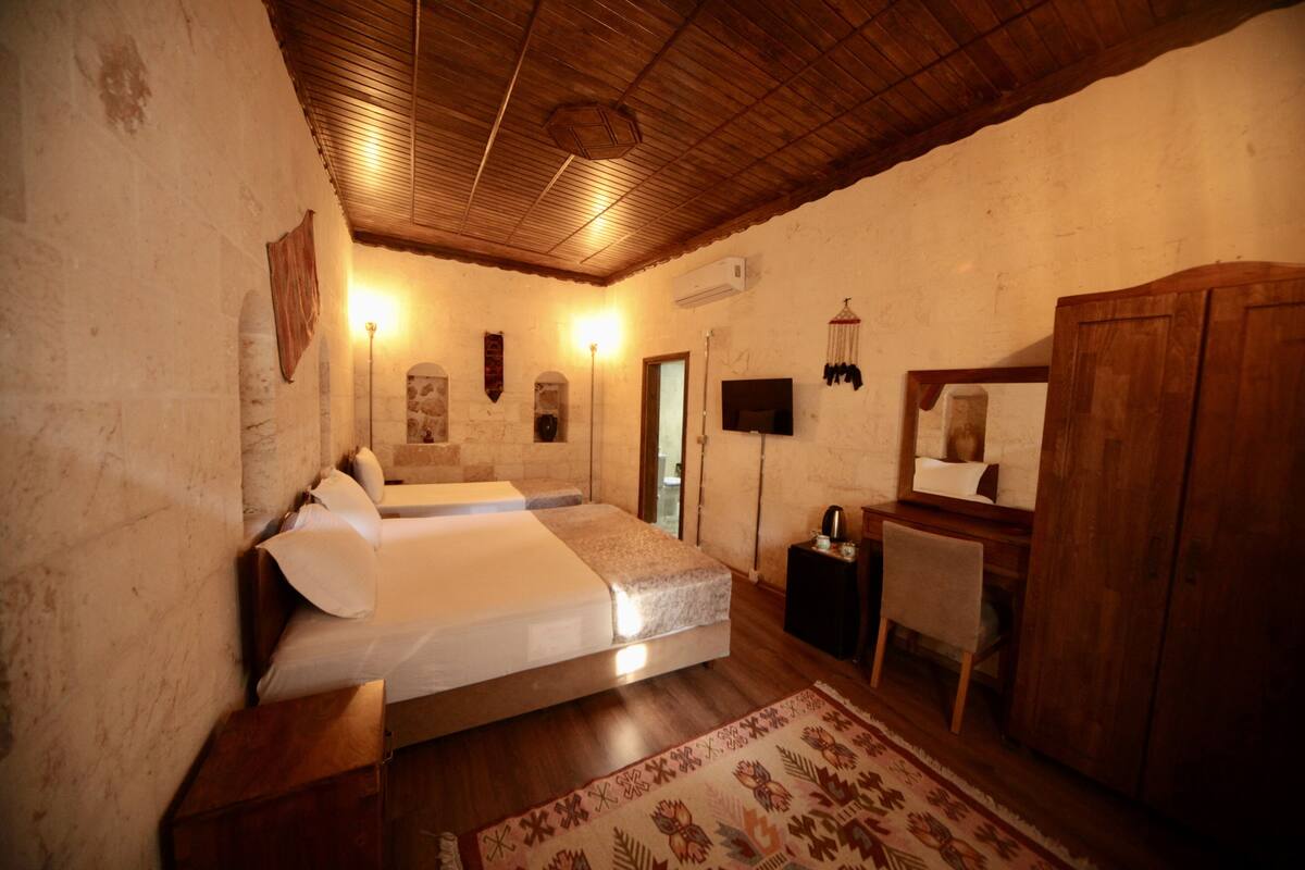 A bedroom with two beds, a wooden wardrobe, a desk with a chair, and a patterned rug.
