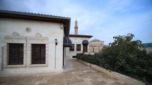 A courtyard with a tiled floor, a building with a minaret, and a tree. - Kaliruha Butik Otel (Sanliurfa)