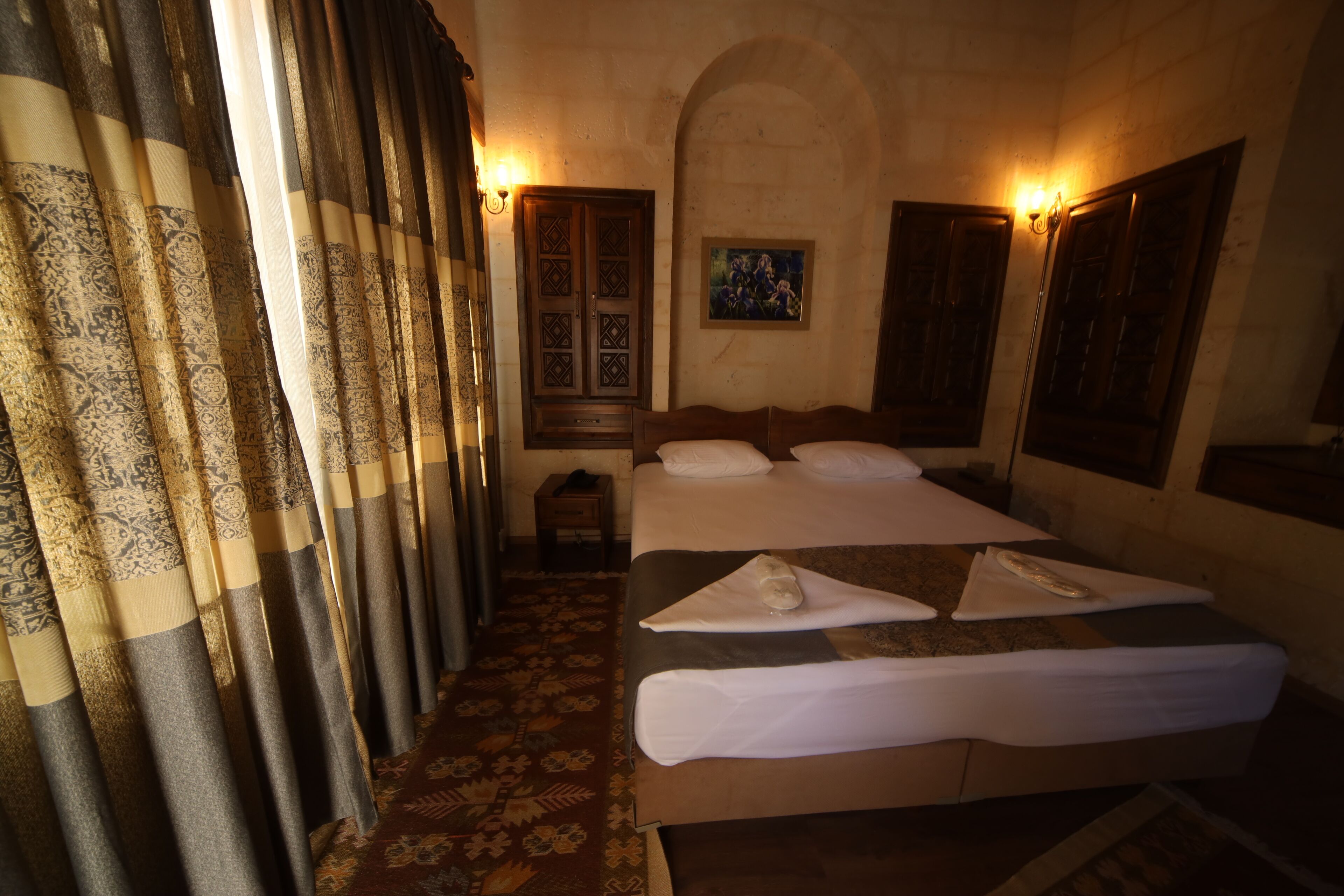A hotel room with a bed, curtains, a painting, and a small table.