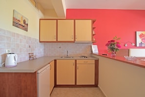 A kitchen with wooden cabinets, a sink, a kettle, and a vase with flowers.