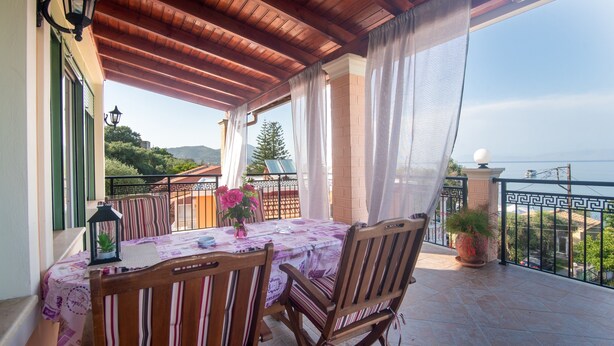 A balcony with a wooden table and chairs, a potted plant, and a view of the sea. - 'Villa Pepy Luxury Apartment' with Mountain View, Garden & Wi-Fi (Corfu)
